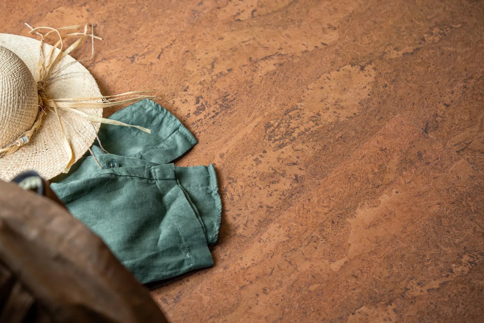 Straw hat and green shirt on brown textured surface with empty space for text or design.
