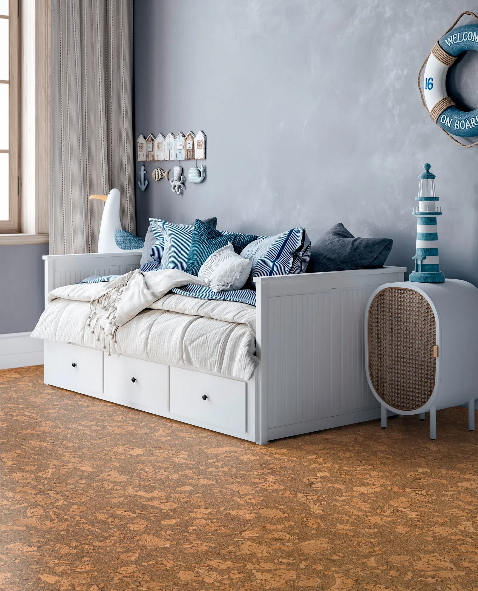 Cozy nautical-themed bedroom with white daybed, blue cushions, marine decor, and cork flooring under natural light.