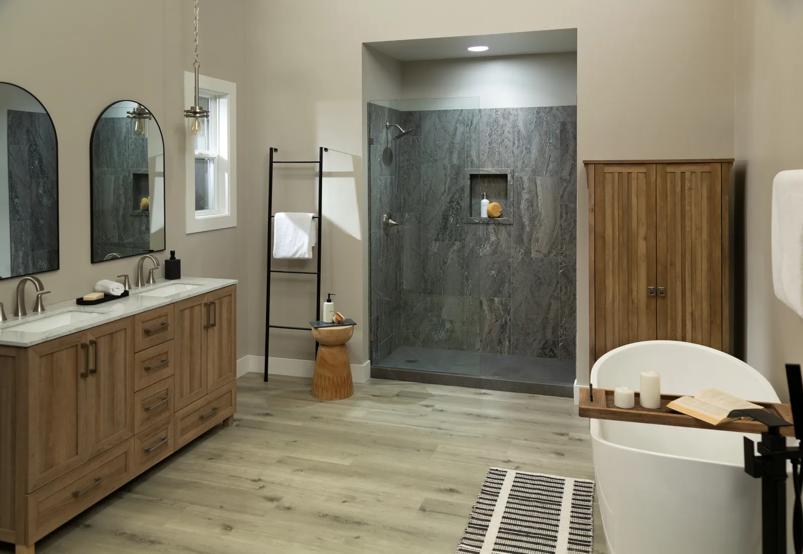 Modern bathroom with wood cabinetry, glass shower, freestanding tub, and light wood flooring.