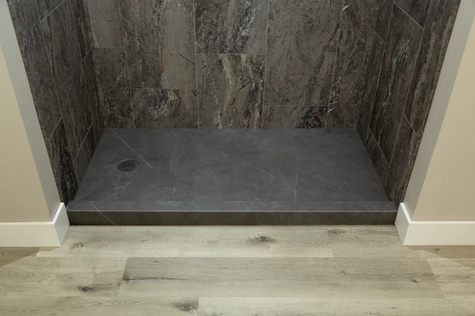 Modern bathroom shower with dark marble tiles and gray stone shower base on wooden floor