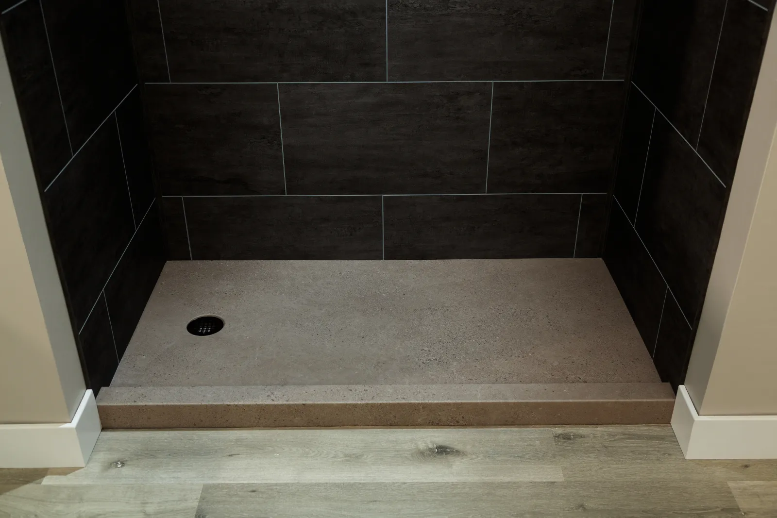 Modern walk-in shower with dark wall tiles and light gray stone shower base with drain
