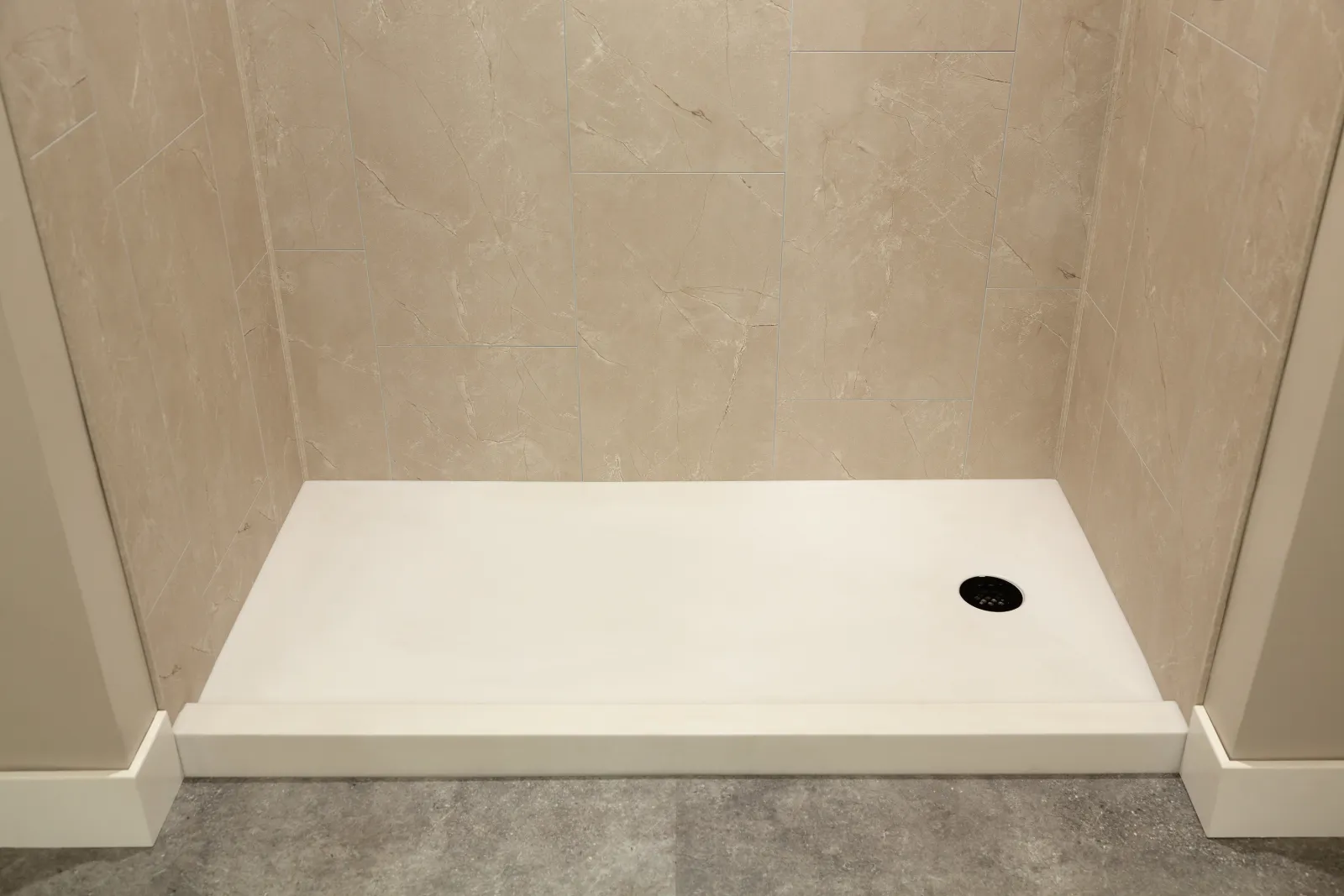 Empty white rectangular shower base with beige tiled walls and gray floor tile in a bathroom.