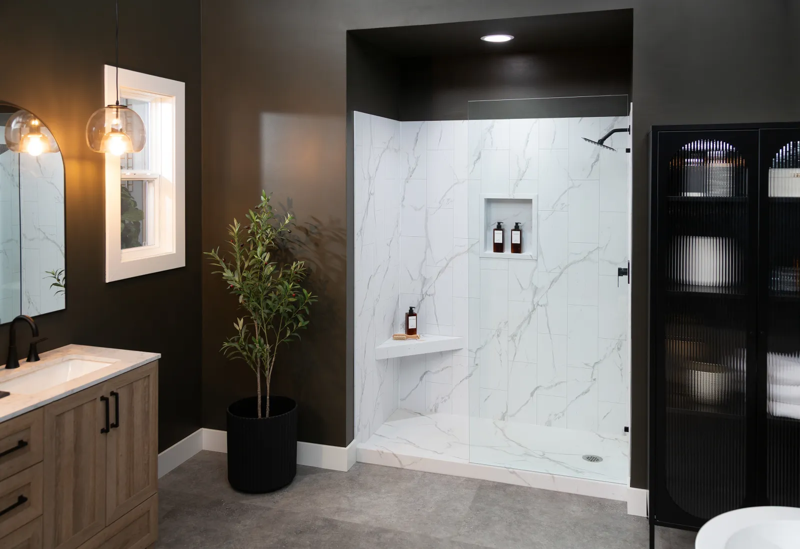 Modern bathroom with glass shower, marble tiles, wooden vanity, black cabinet, and indoor plant.