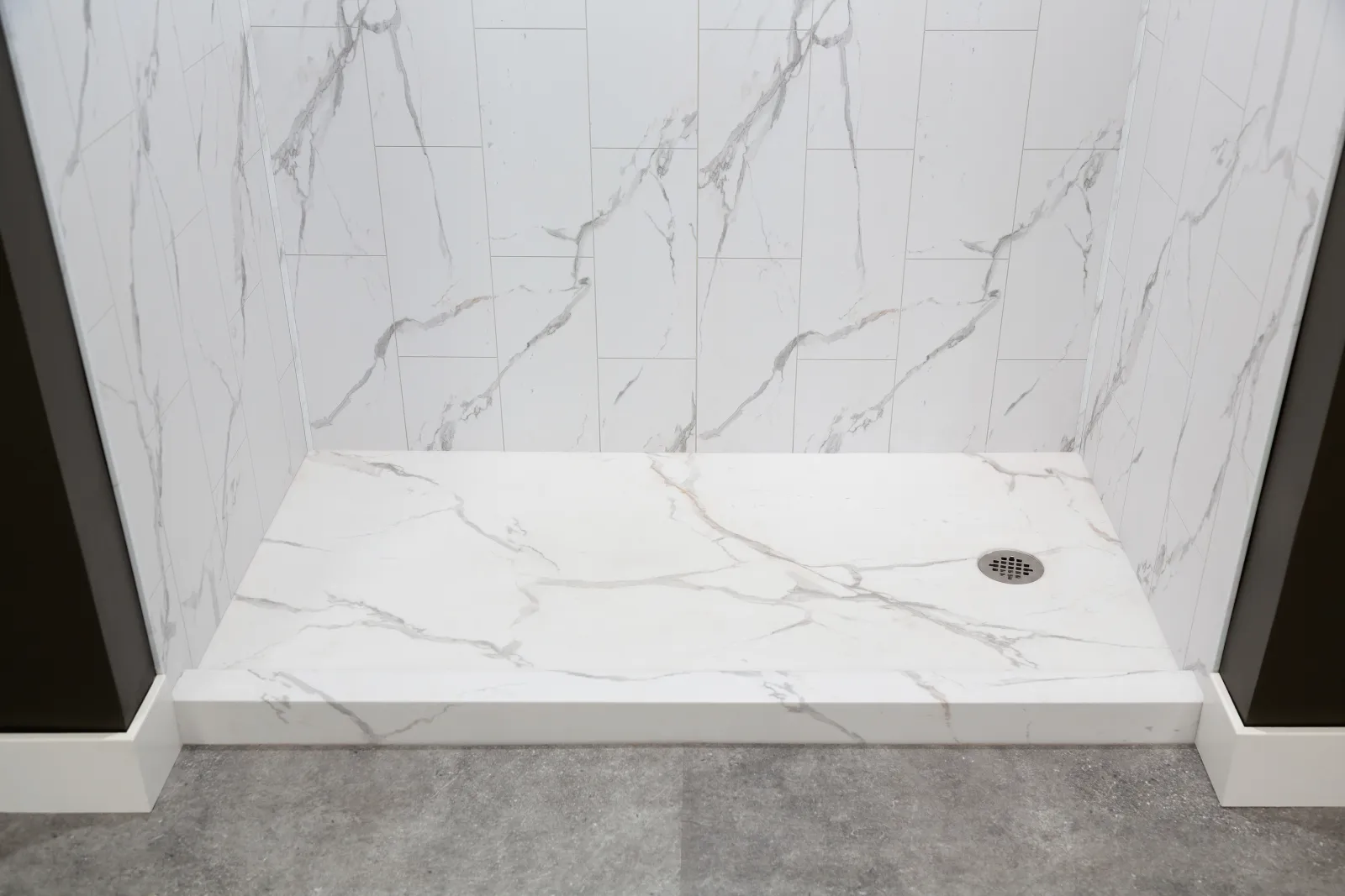 White marble shower area with veined tiles, a built-in drain, and gray textured floor outside the shower