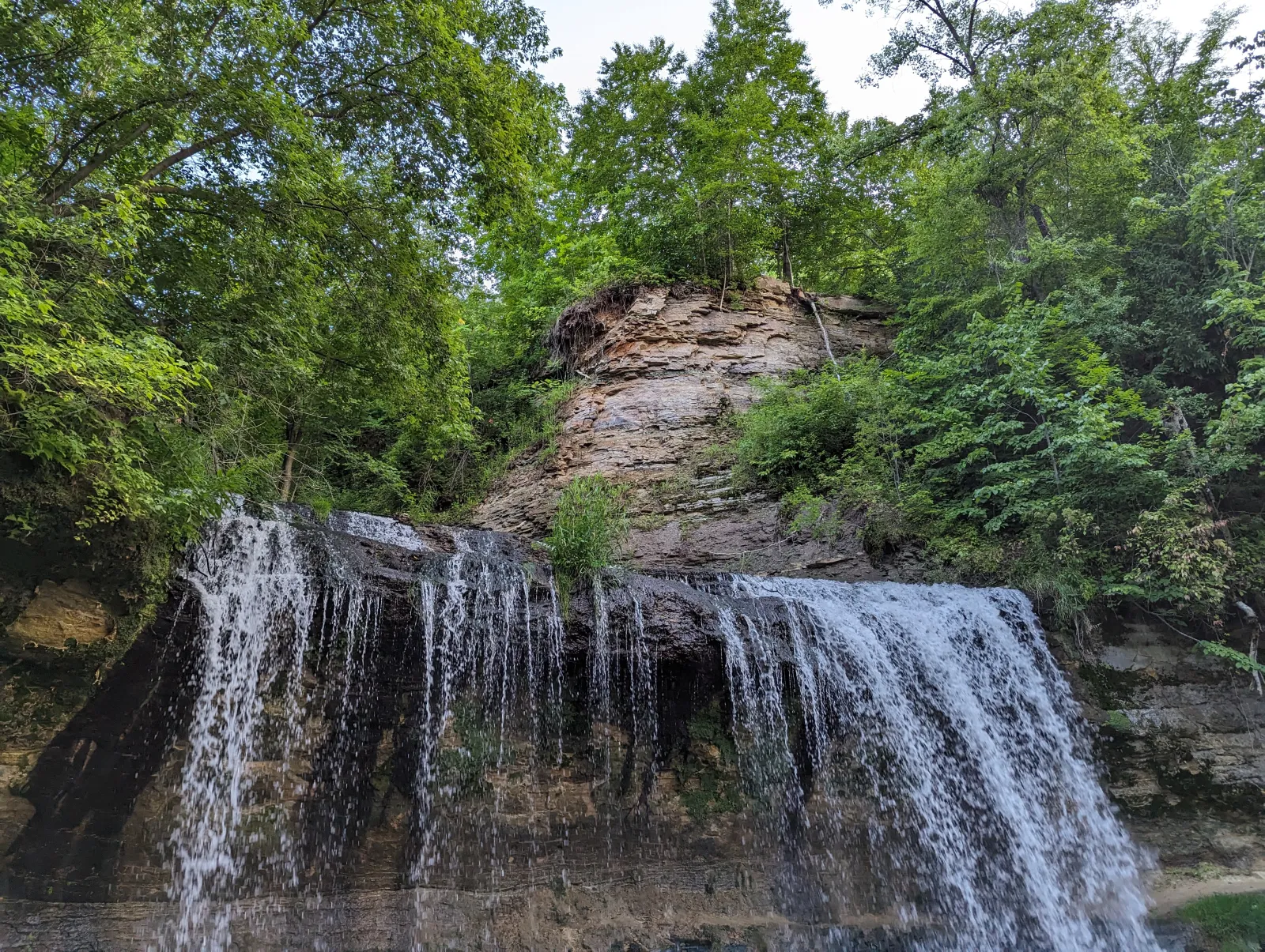 Waterfall cascading over rocky cliffs surrounded by lush green forest under a clear sky.