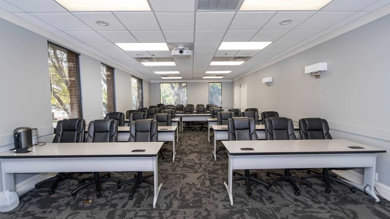 Modern conference room with black leather chairs, white desks, projector, and large windows letting in natural light.