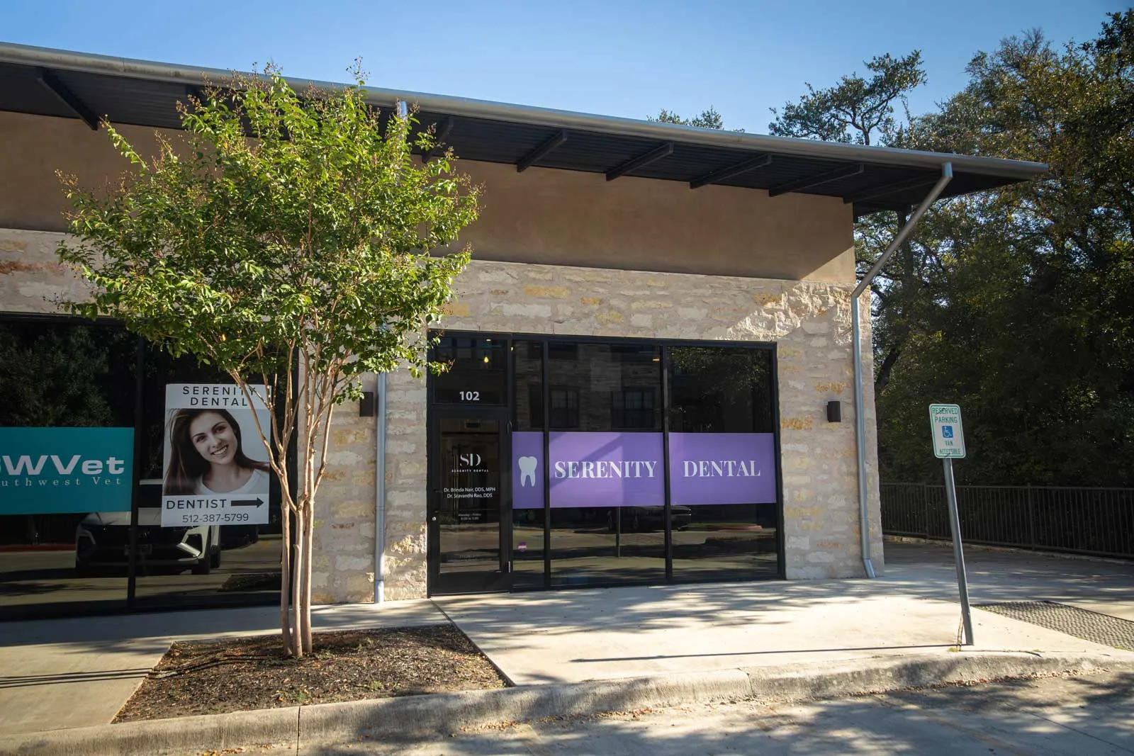 Exterior view of Serenity Dental clinic with stone facade and purple signage on glass doors under blue sky.