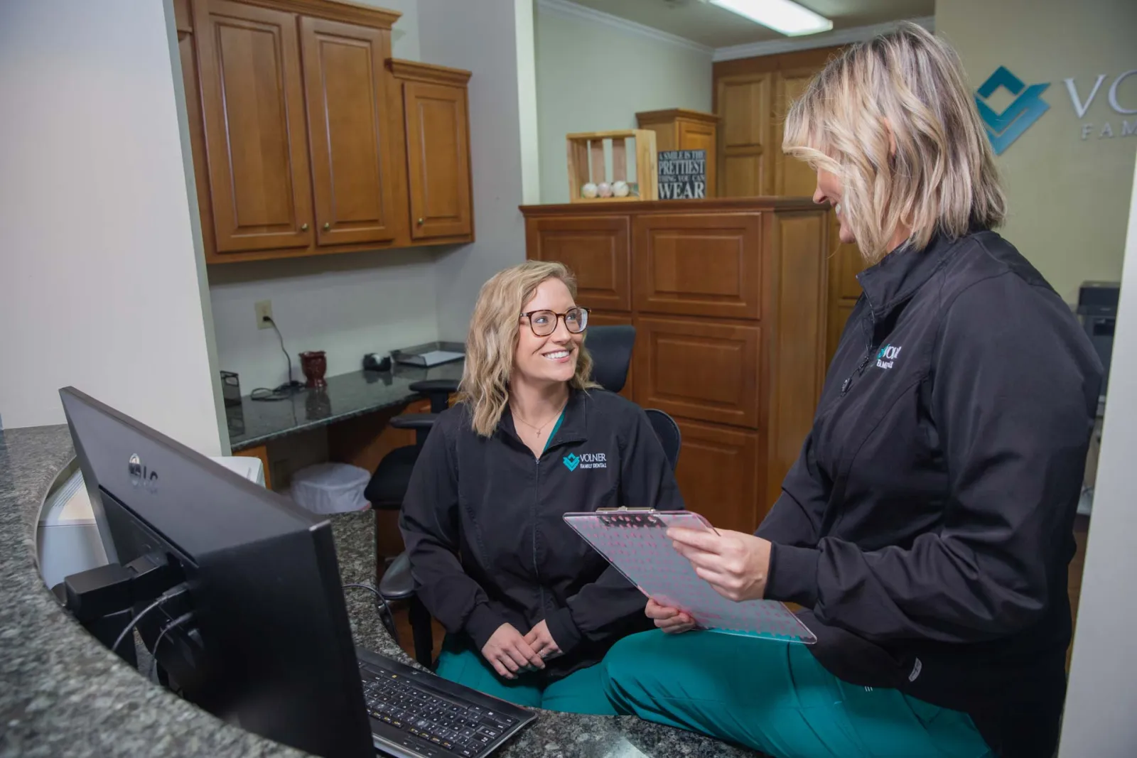 Two female medical professionals in black jackets discussing patient files in a modern clinic office.