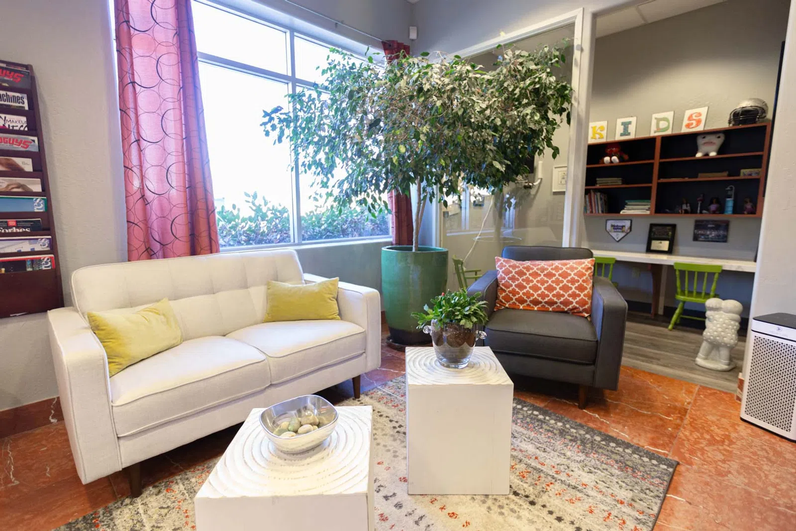 Modern living room with white sofa, gray armchair, green plants, and bright natural light from large window.