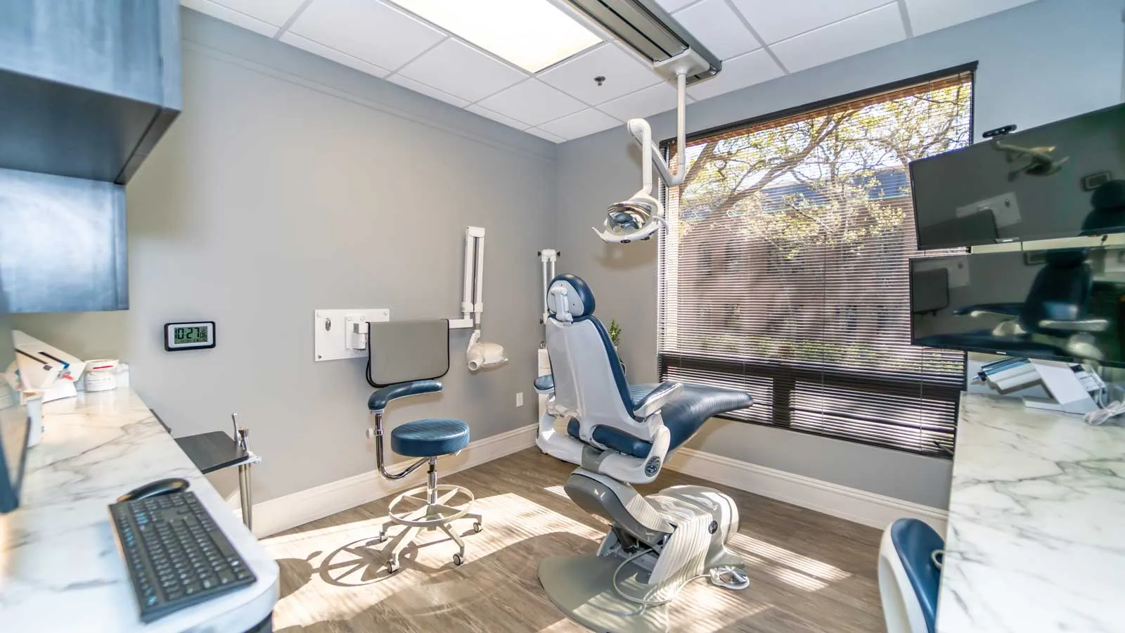 Modern dental office with reclining chair, stool, equipment, and large window with blinds.