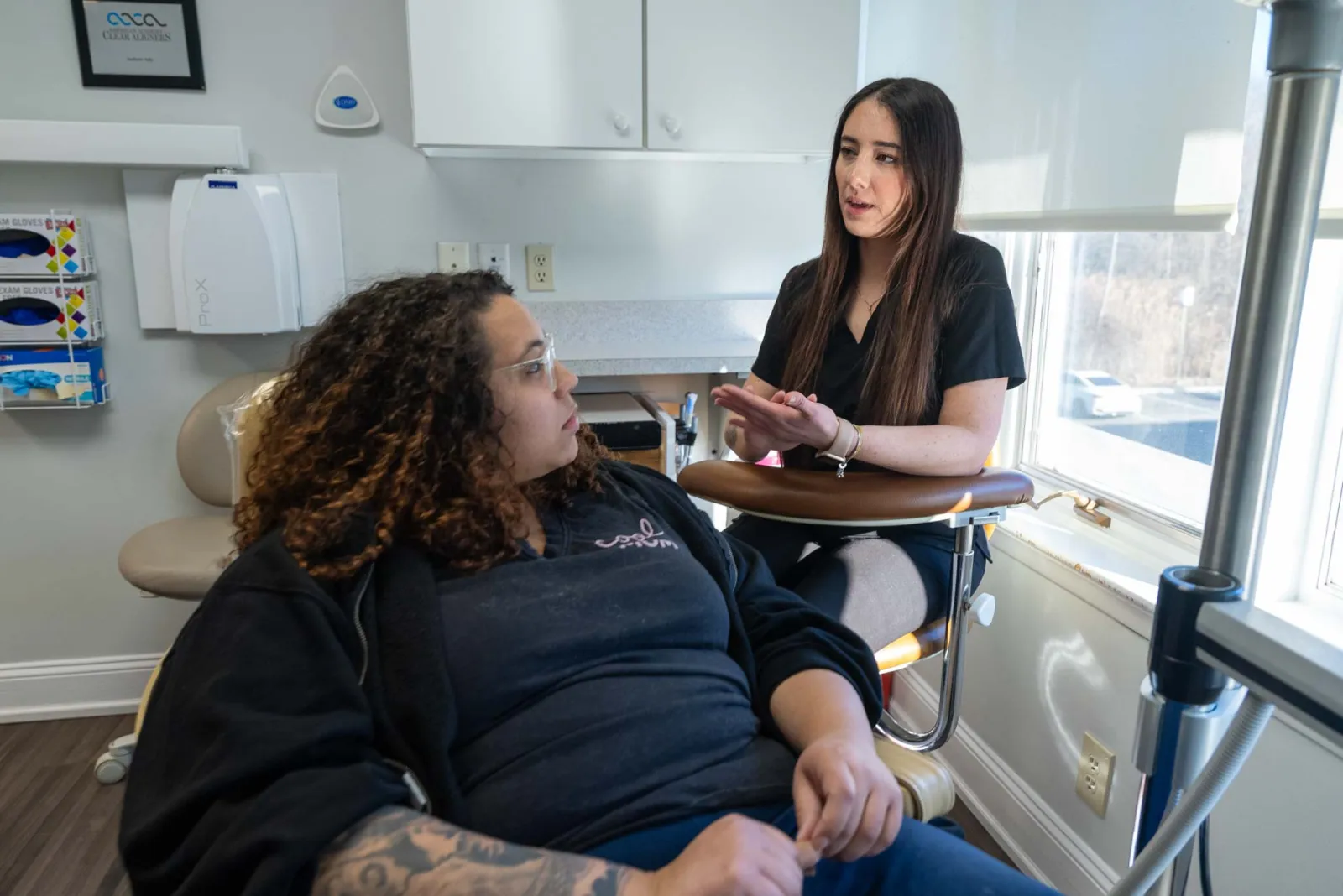 Two women engaged in a discussion in a bright clinical or office setting near a window
