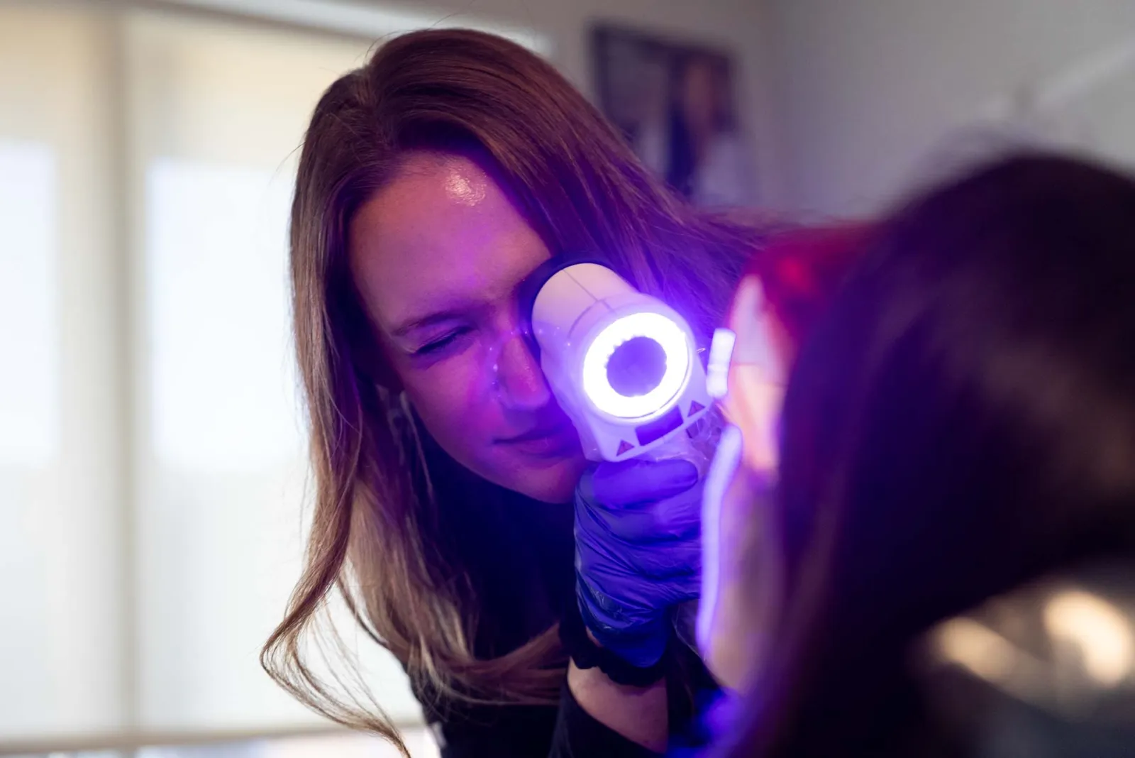 Healthcare professional using a dermatoscope to examine a patient's skin under bright light in a clinical setting
