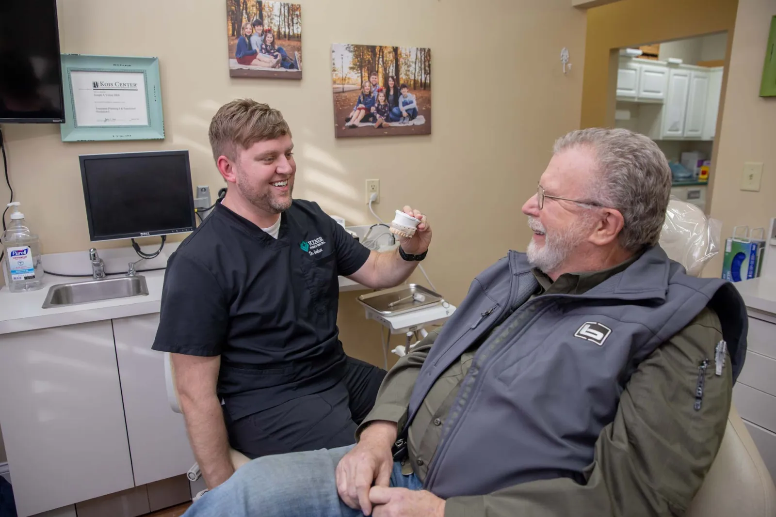 Dentist showing dental mold to a smiling elderly male patient in a bright dental office.