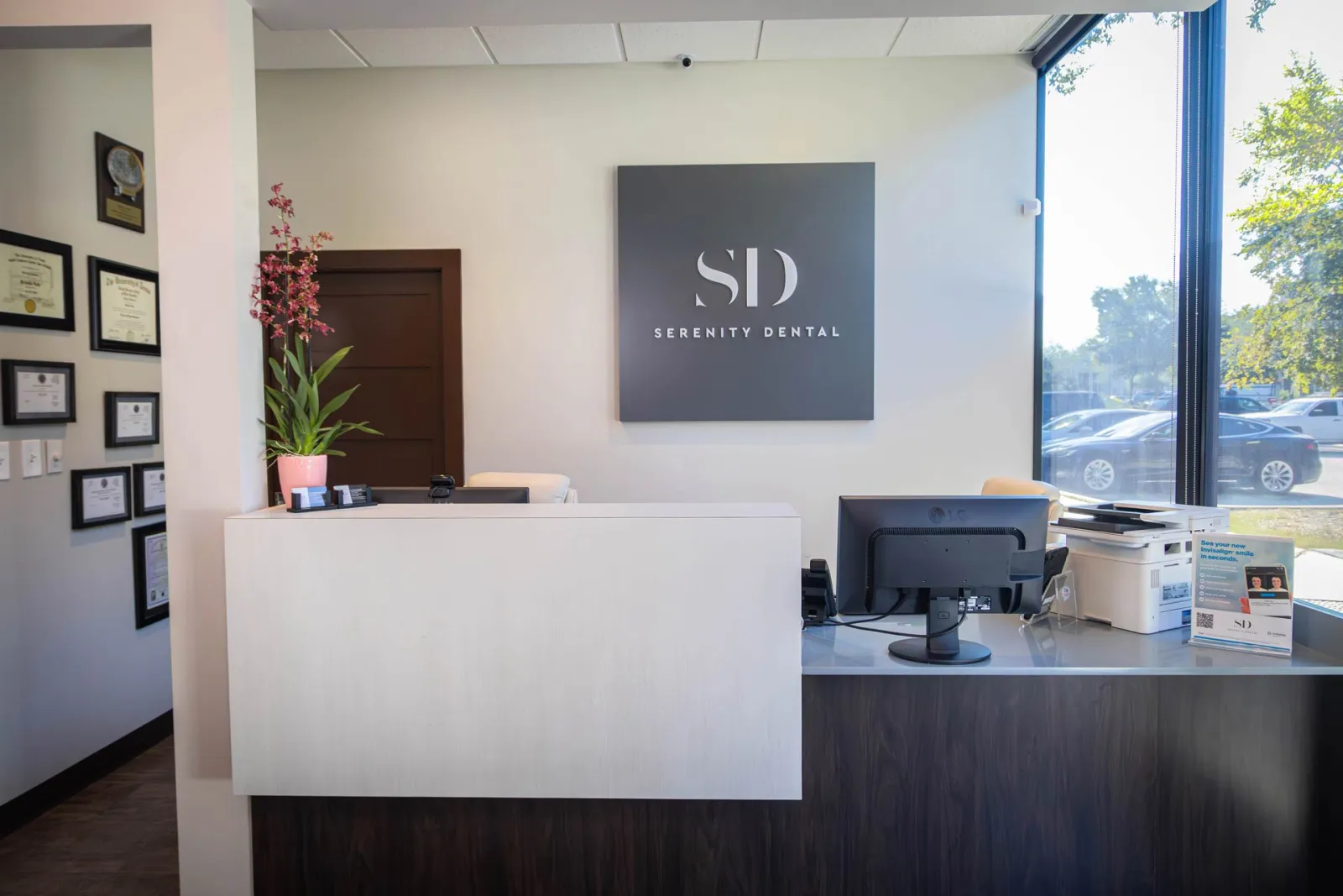 Modern dental office reception with Serenity Dental sign, certificates, computer, and large window with outdoor view.