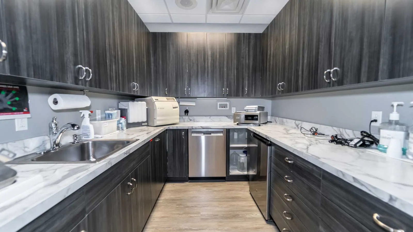 Modern laboratory kitchenette with dark wood cabinets, marble countertops, stainless steel appliances, and medical supplies.