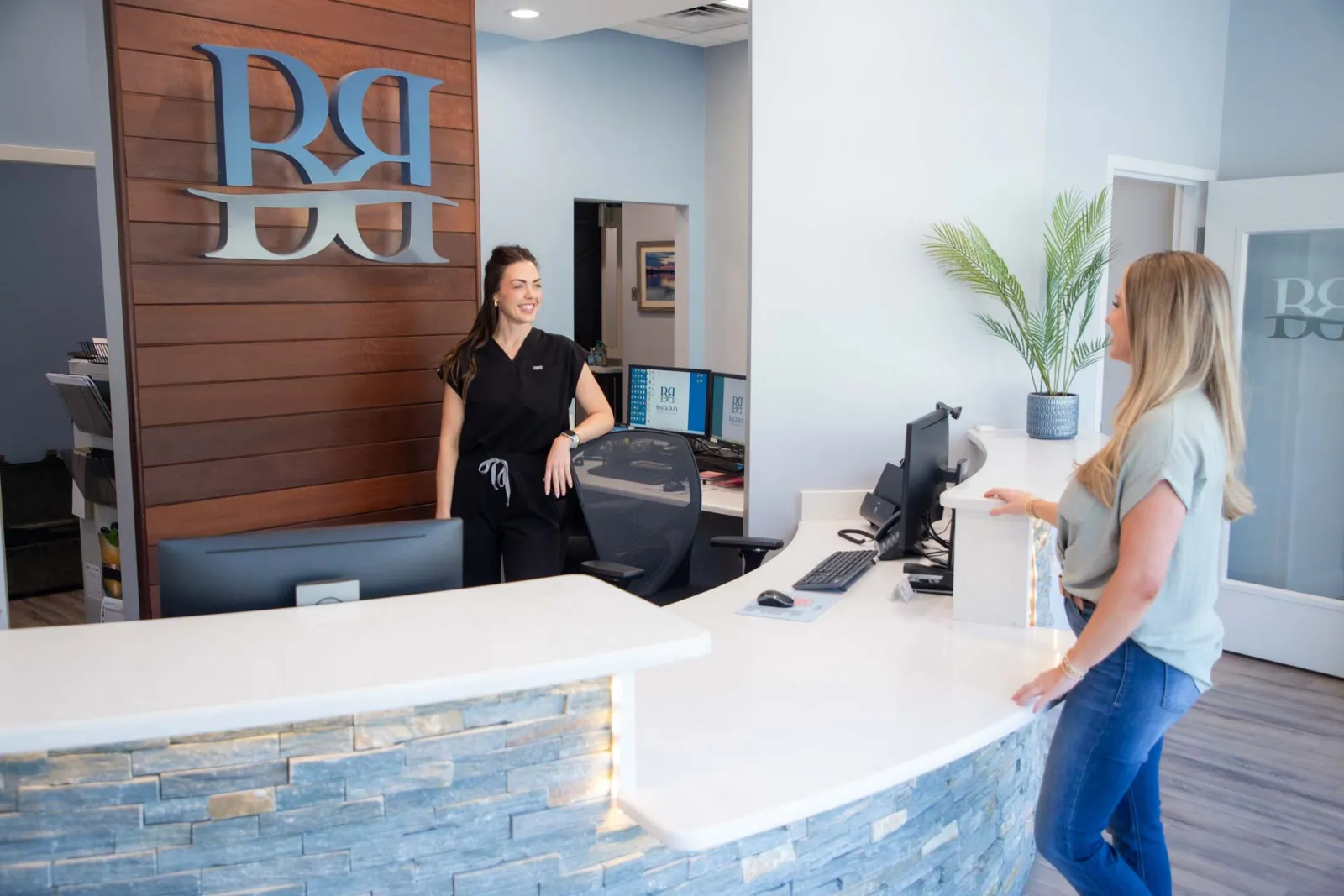 Reception area with smiling receptionist and client at curved white desk in modern office lobby.