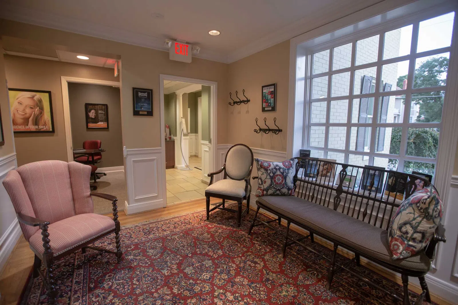 Cozy waiting room with vintage armchairs, a wooden bench with patterned cushions, and a large window letting in natural light.