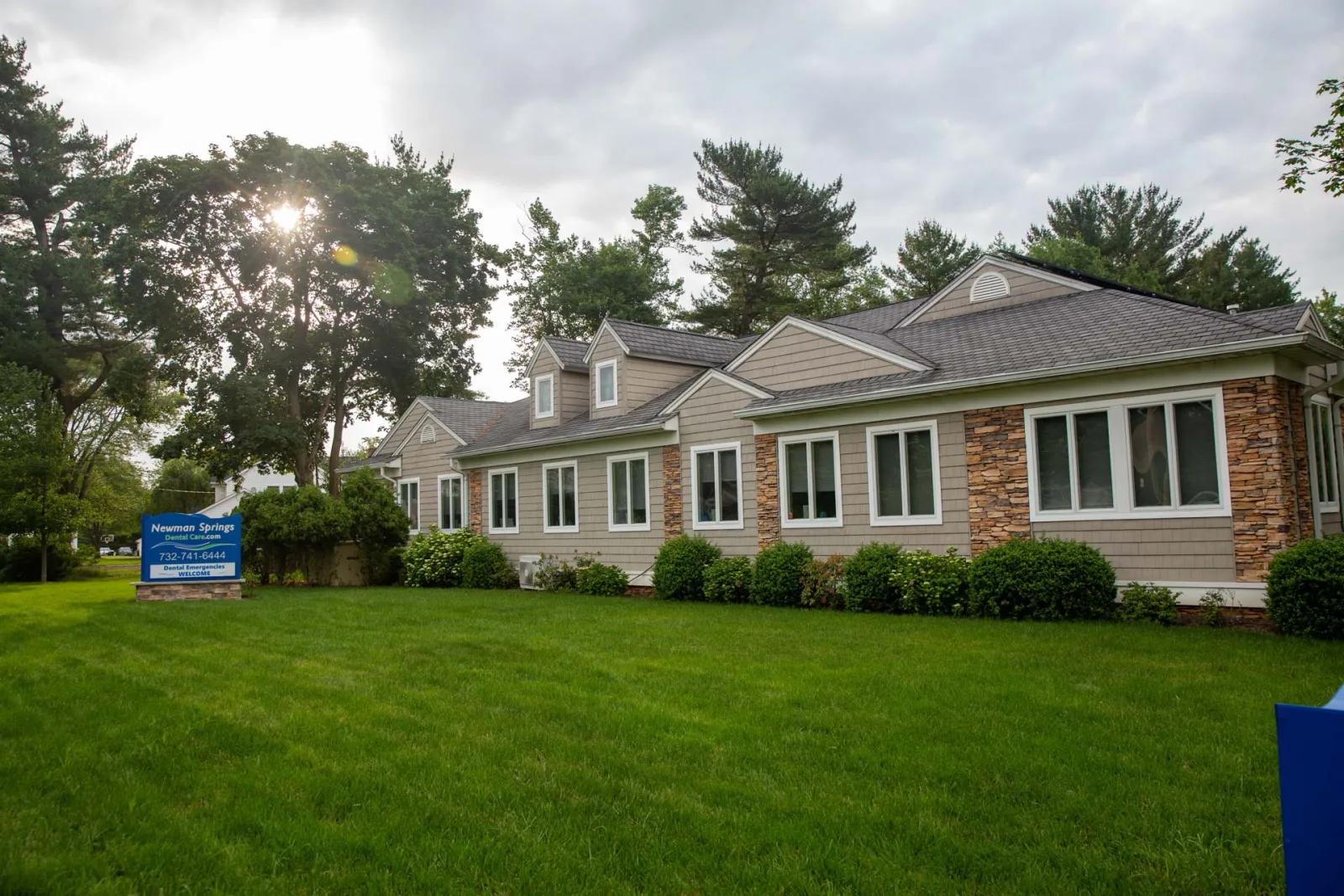 Modern single-story building with stone and siding exterior surrounded by green lawn and trees under cloudy sky.