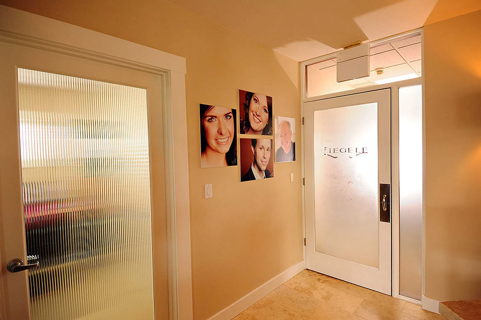 Bright hallway with frosted glass doors and portrait photos on beige walls in a professional office setting