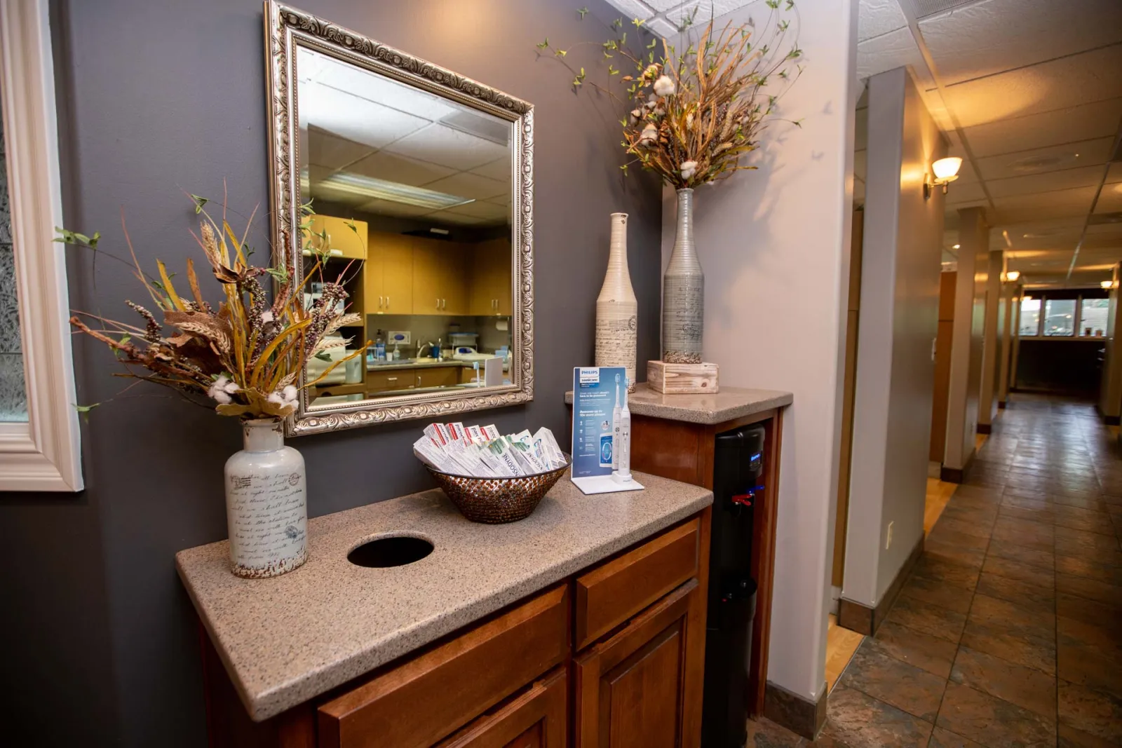 Reception area with decorative vases, mirror, basket of cards, and hallway with tile floor in a professional office.
