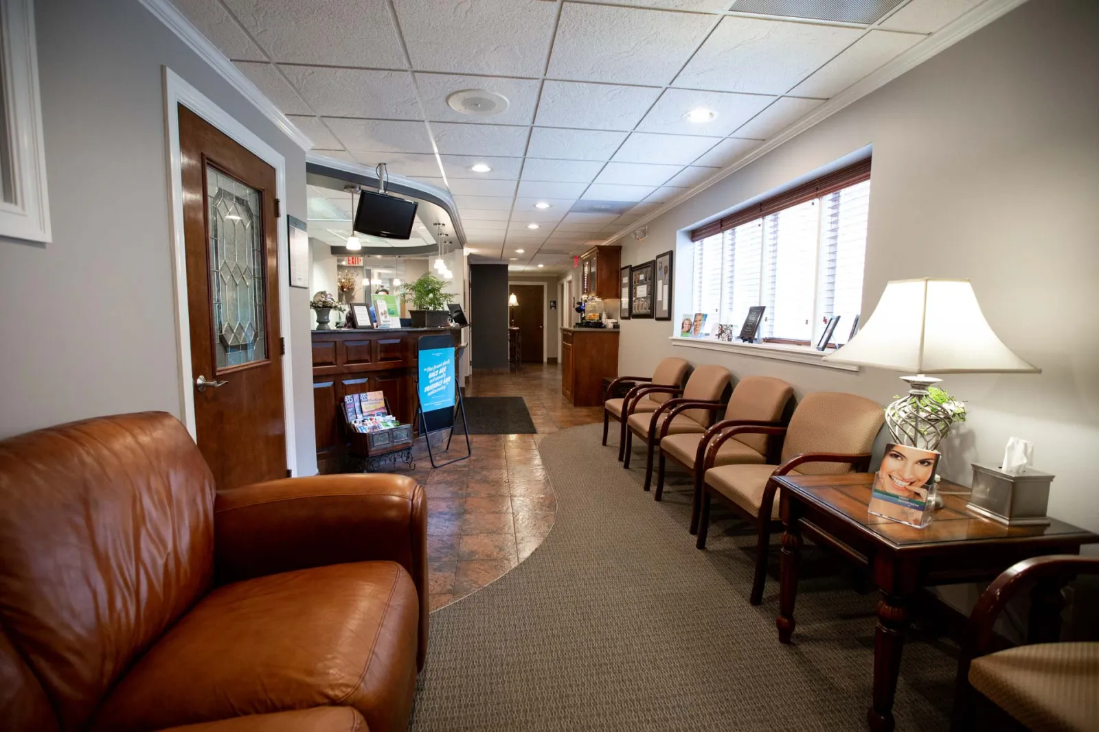 Bright and welcoming medical office reception area with brown leather sofa, chairs, and wooden desk under warm lighting.