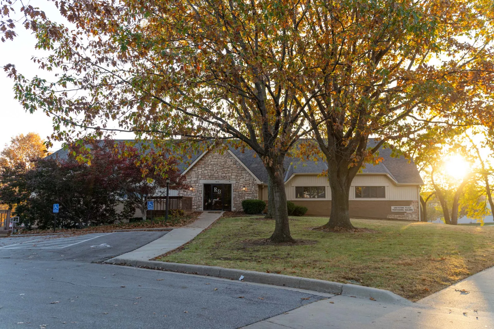 Community center building with stone façade, autumn trees, and sunset lighting on a clear day