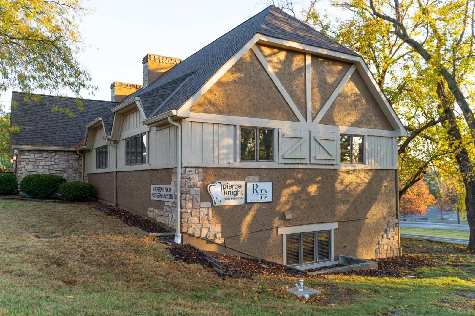 Exterior view of a beige stone and stucco dental office building surrounded by autumn trees and grass.