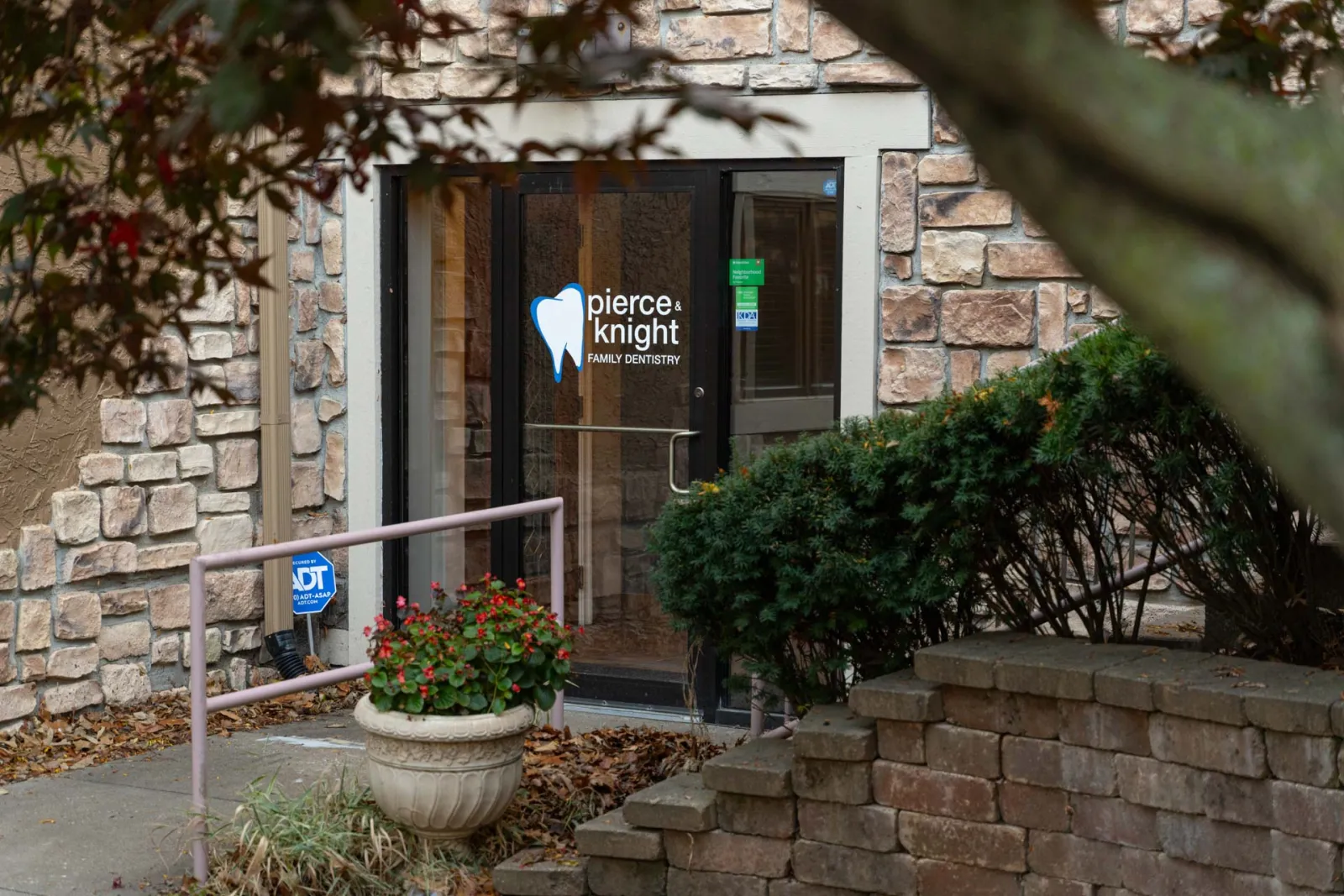Entrance to Pierce & Knight Family Dentistry with stone walls, plants, and a glass door with signage.