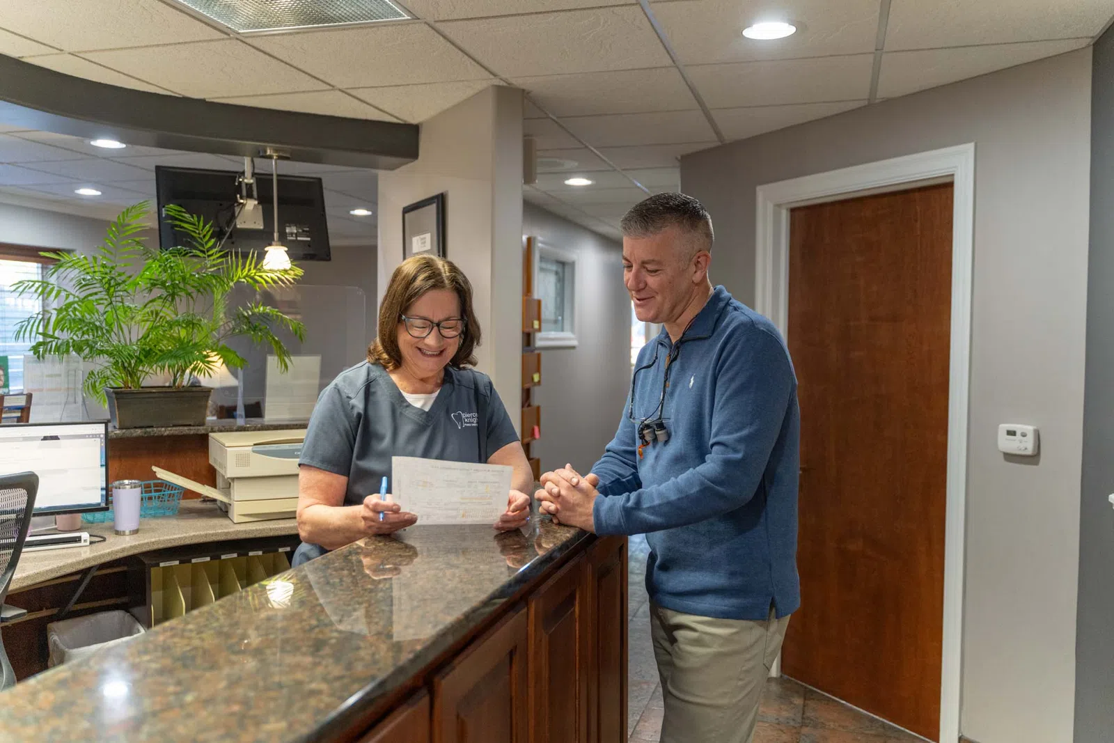 Smiling receptionist assists male patient with paperwork at dental office front desk
