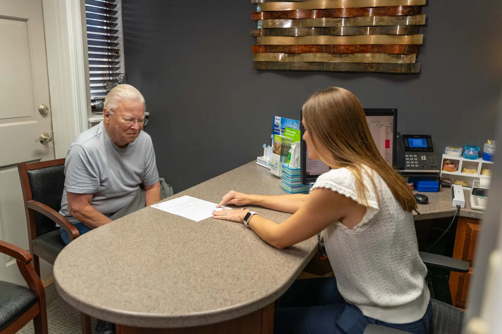 Older man consulting with a female professional at a desk in an office setting with documents and computer.