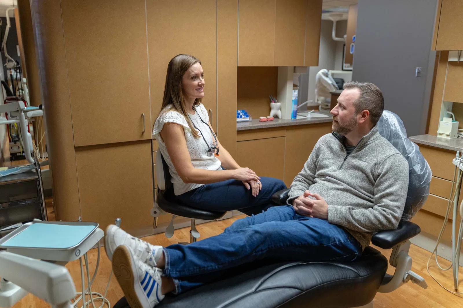 Dentist and male patient having a conversation in a dental office with equipment visible around.