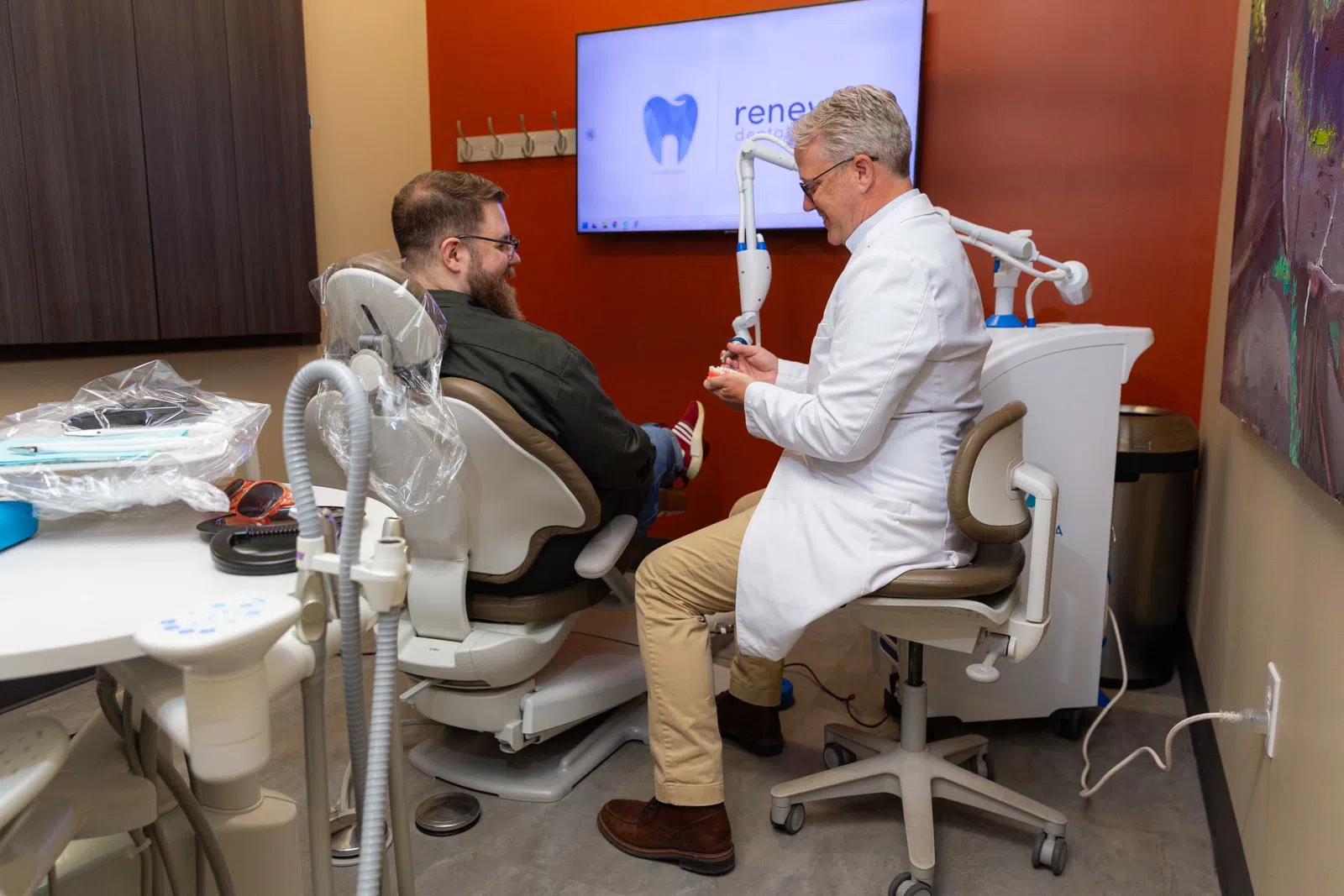 Dentist in white coat consulting smiling male patient sitting in dental chair in modern clinic room.