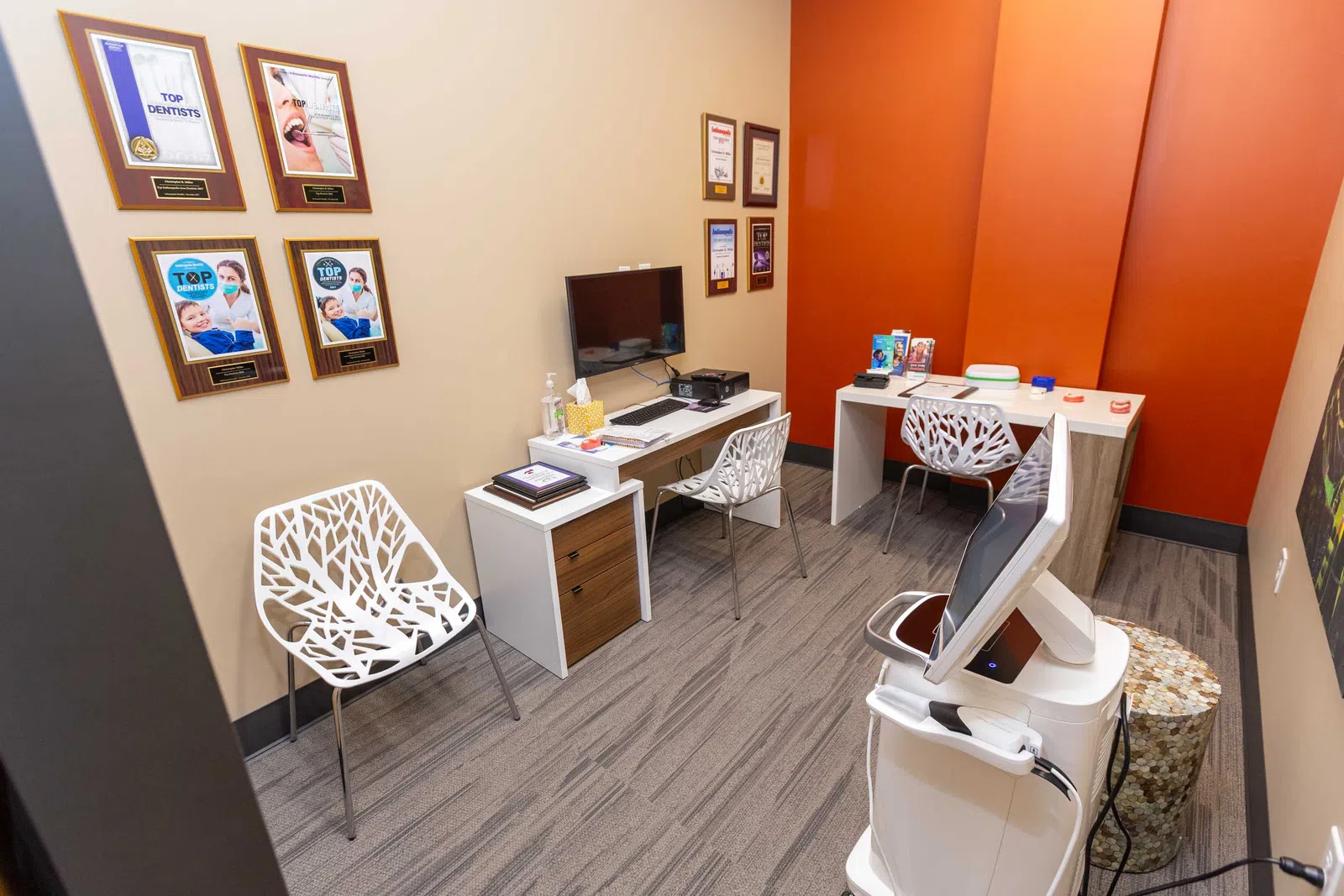 Modern dental office consultation room with contemporary chairs, computer station, and award plaques on wall.