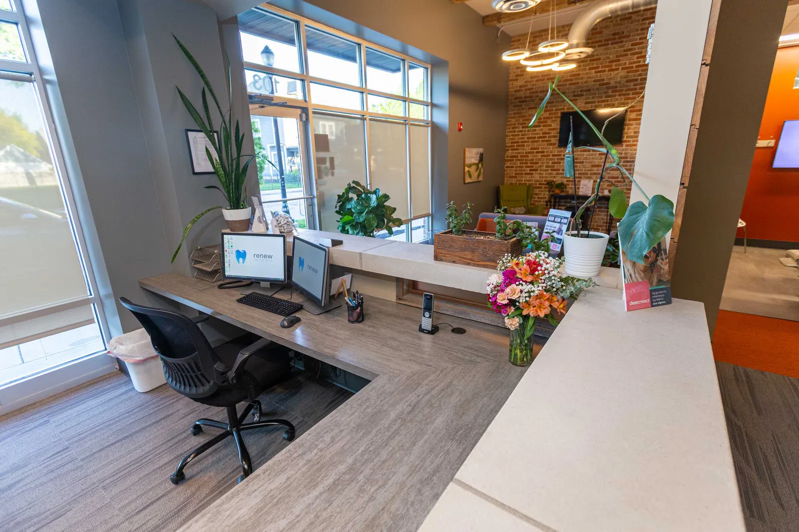 Modern dental office reception with computers, flowers, plants, and natural light from large windows