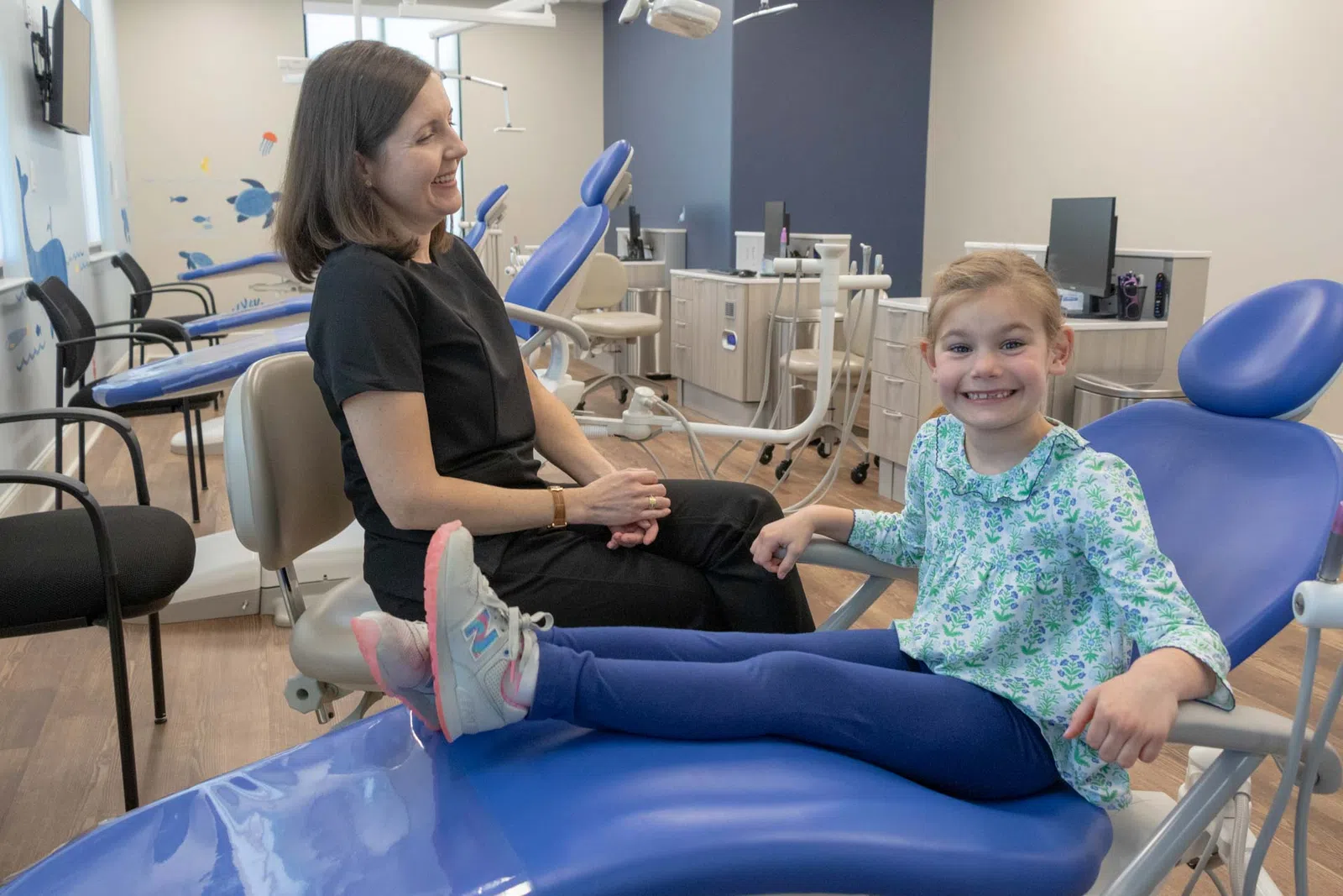 Smiling young girl sitting on dental chair with female dentist in modern clinic room