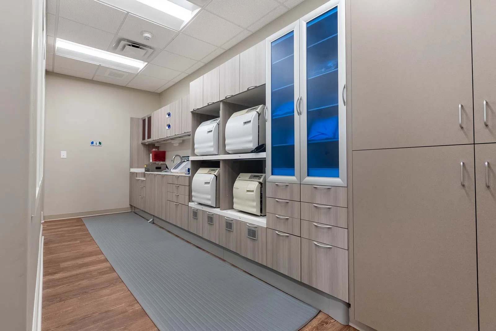 Modern dental sterilization room with autoclaves, cabinets, and wood flooring under fluorescent lighting