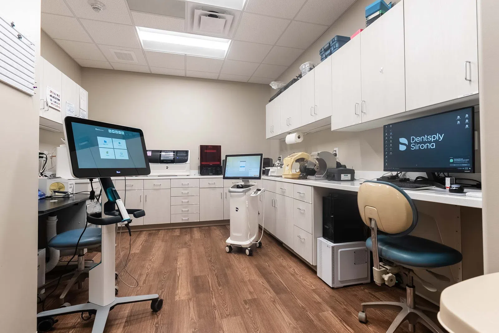 Modern dental lab with digital equipment, workstations, and wooden flooring in a clean, organized setting