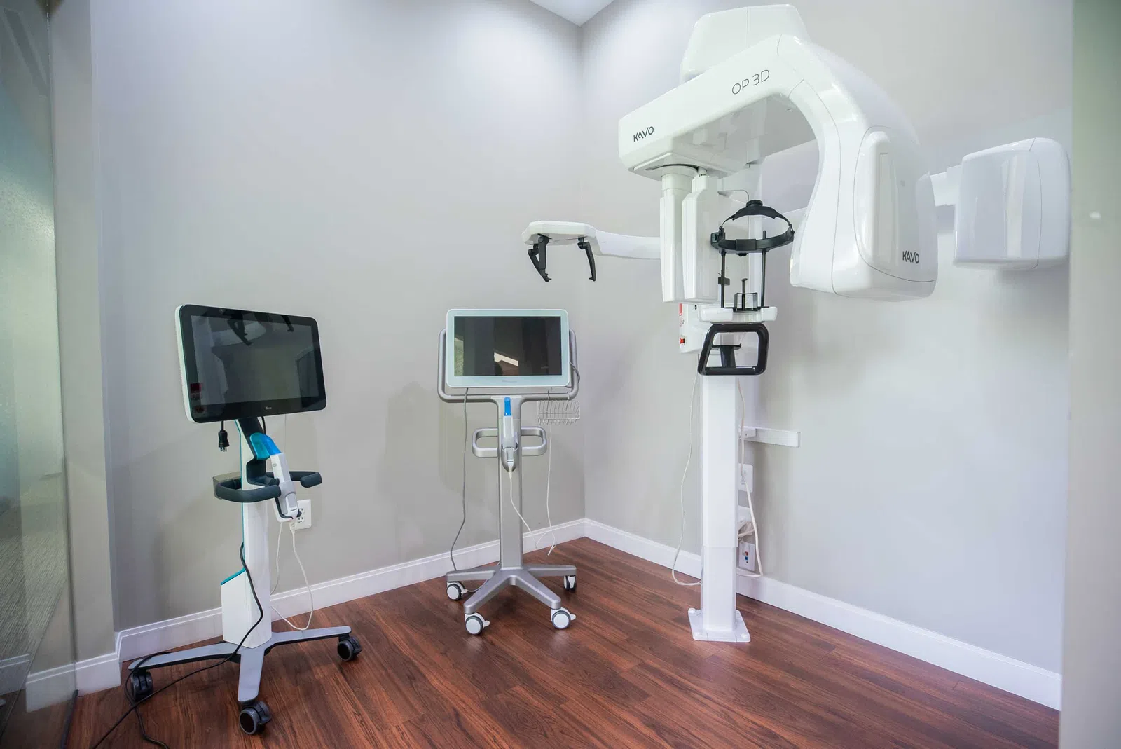 Dental imaging room with a 3D panoramic X-ray machine and two computer monitors on mobile stands.