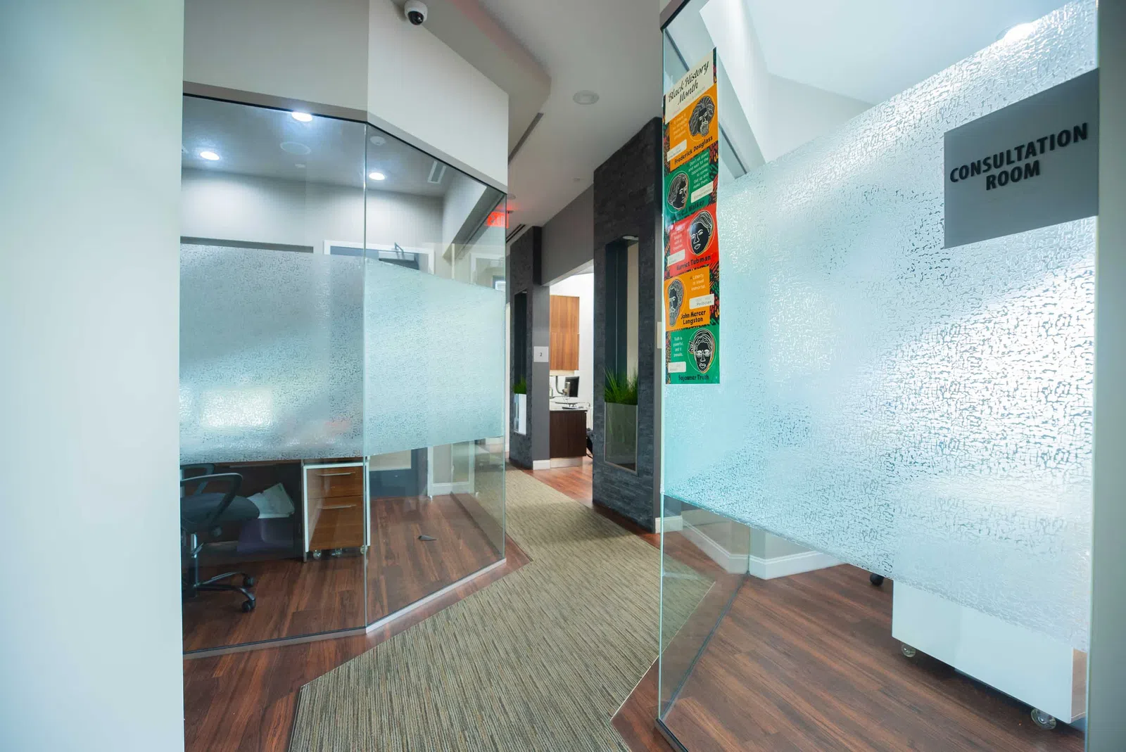 Modern office hallway with frosted glass consultation rooms and wooden flooring in a professional setting