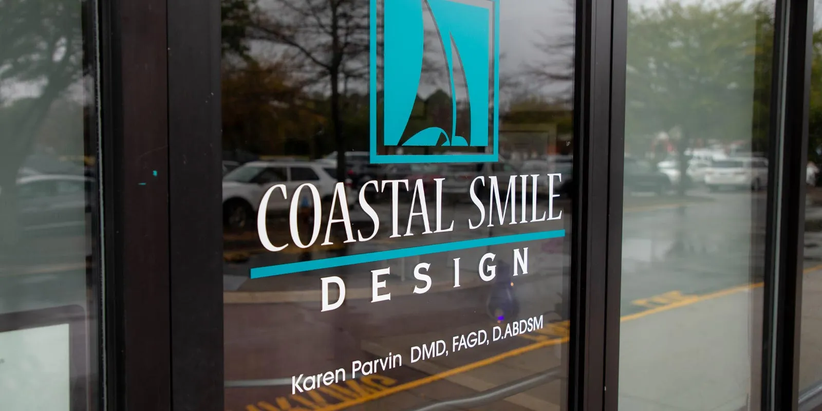 Coastal Smile Design logo with sailboat icon and dentist Karen Parvin's credentials on glass door.