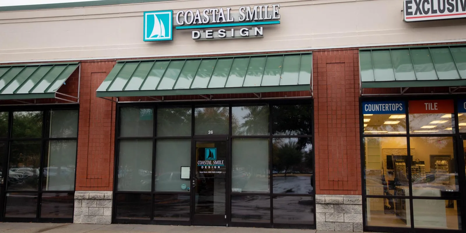 Storefront of Coastal Smile Design with teal sailboat logo and green awnings over glass windows and door