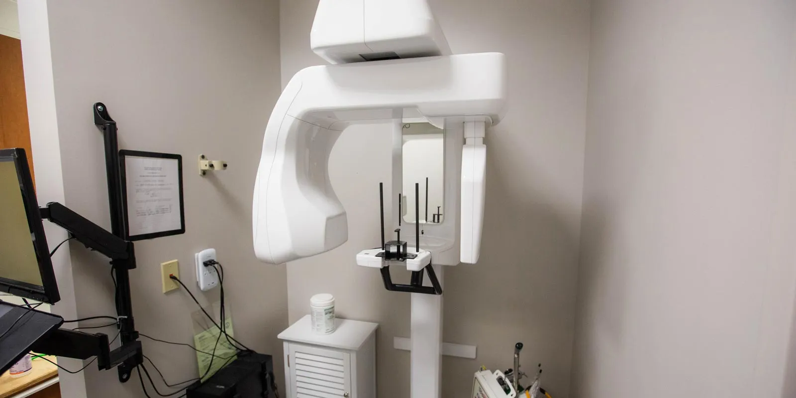 Modern dental X-ray machine in a clean clinic corner with computer setup and imaging equipment.