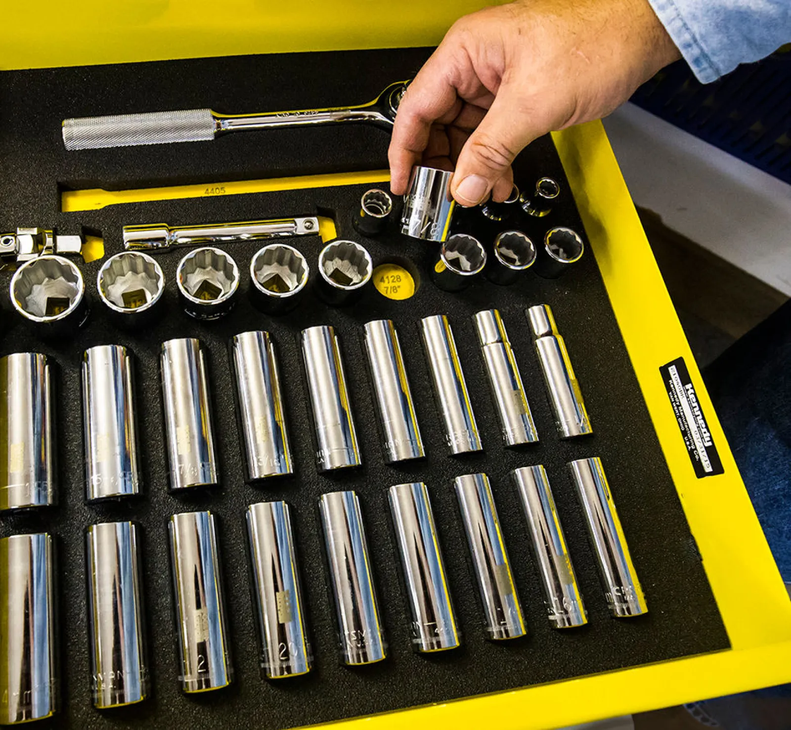 Hand holding a chrome socket from a set of organized shiny sockets and tools in a yellow foam-lined case.