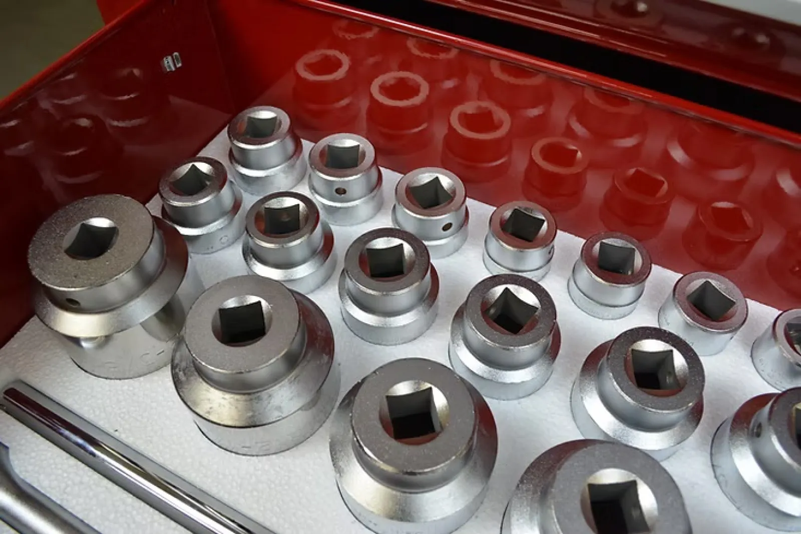 Set of shiny metal socket wrench heads organized in a red tool case with reflections on their surfaces.