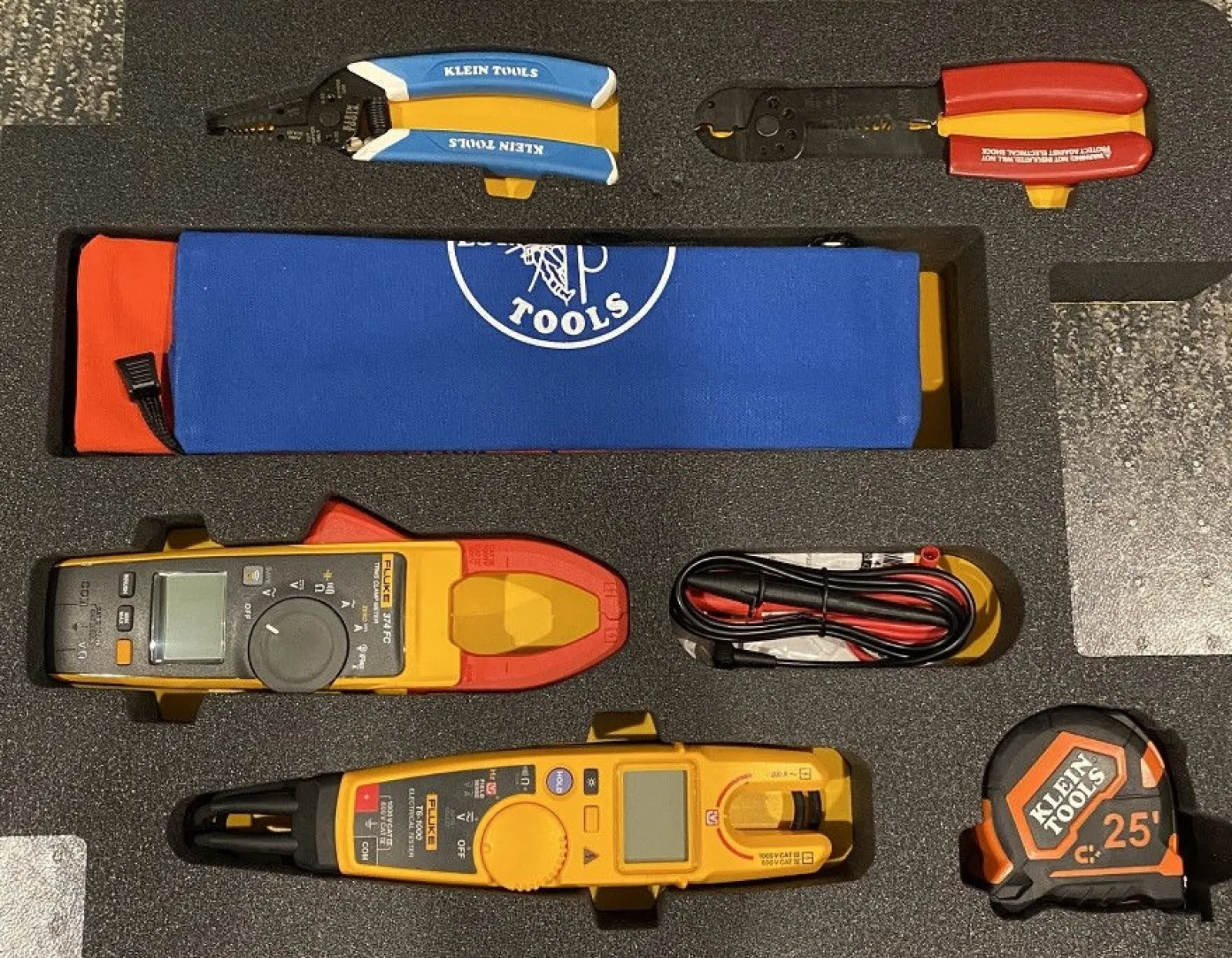 Set of Klein Tools including wire strippers, crimpers, multimeters, and measuring tape in foam case