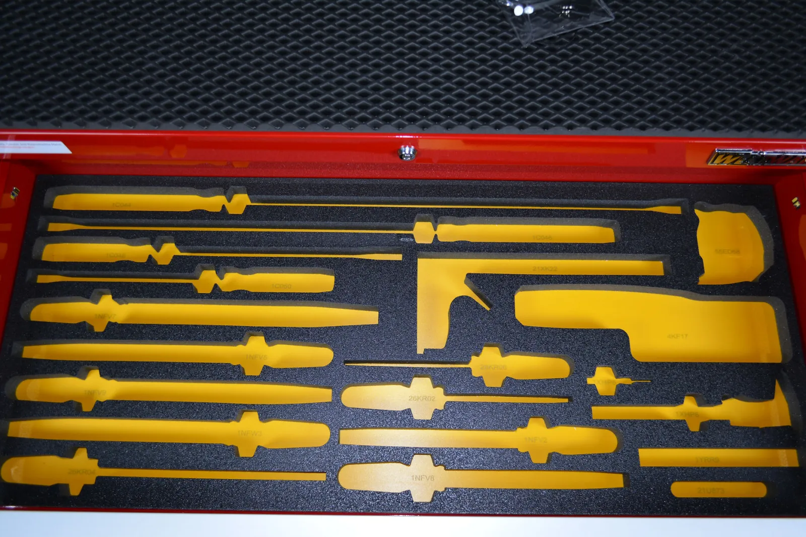 Yellow tool silhouettes arranged in black foam inside a red toolbox drawer with a textured black background.