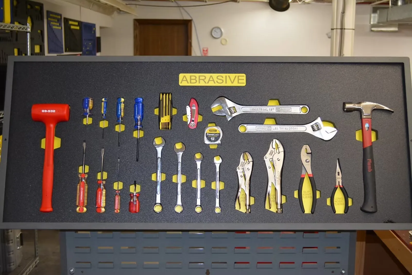 Organized wall-mounted tool board labeled Abrasive with hammers, screwdrivers, wrenches, pliers, and measuring tape