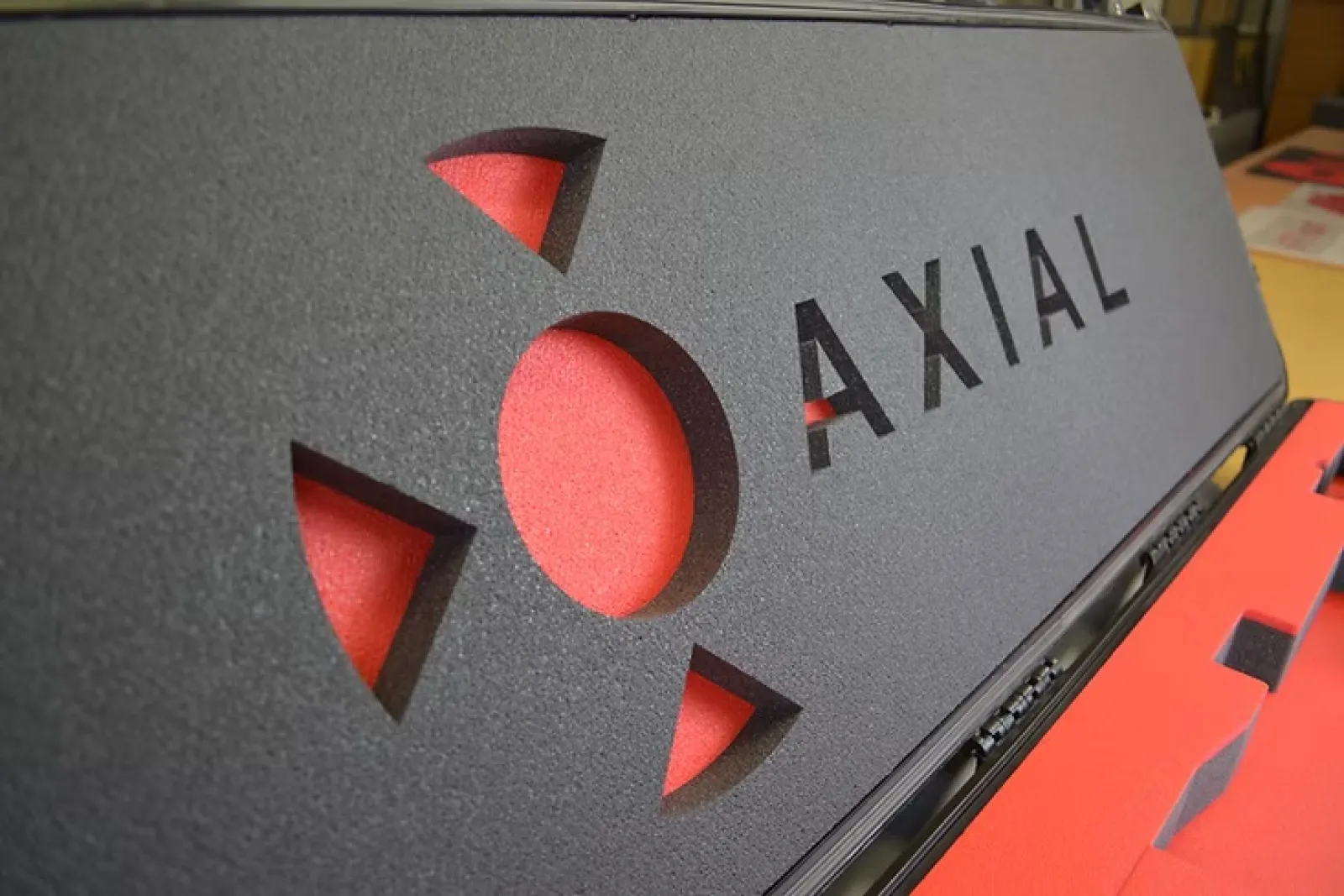 Close-up of black foam casing with red interior and cutout text Axial on the side of a protective case.