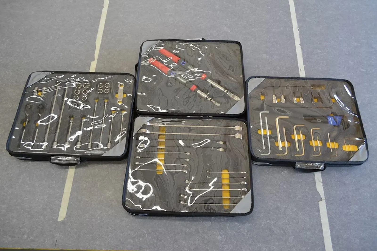 Four black toolkits with transparent covers displaying various precision tools including screwdrivers and hex keys.