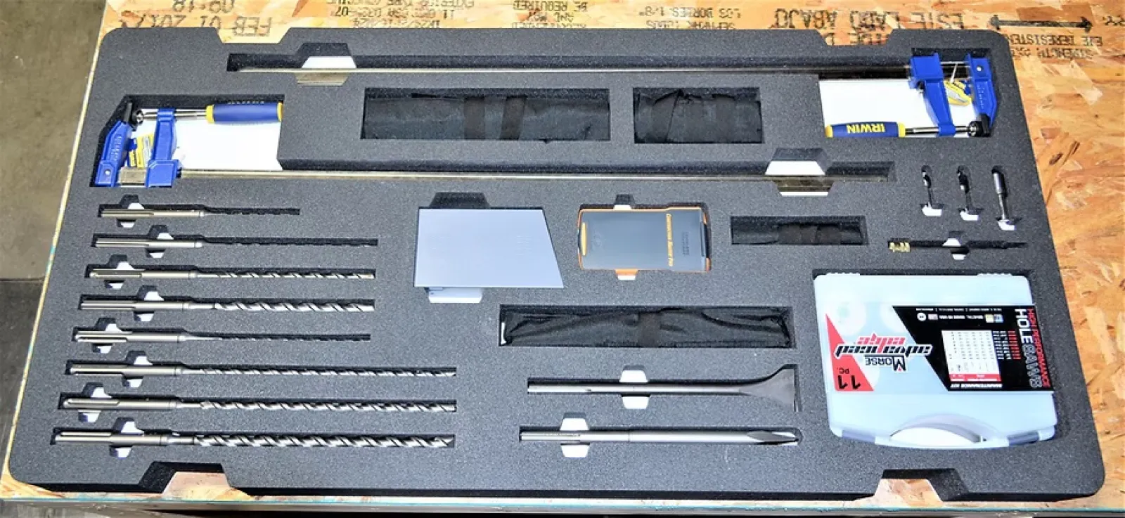 Organized foam case containing drill bits, clamps, and precision tools on wooden surface.